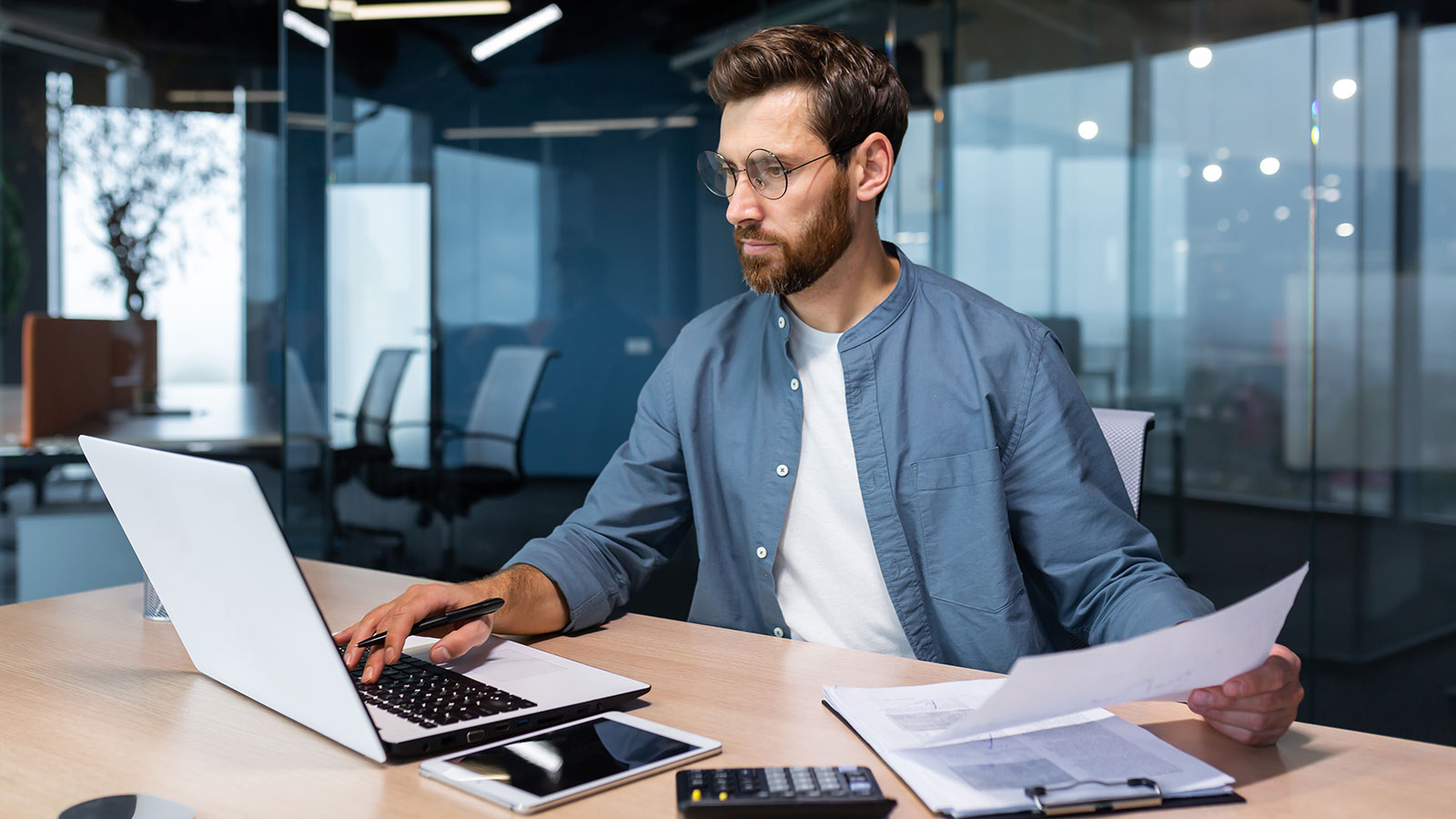 A serious young man accountant, financier, analyst, auditor sits in the office at the table