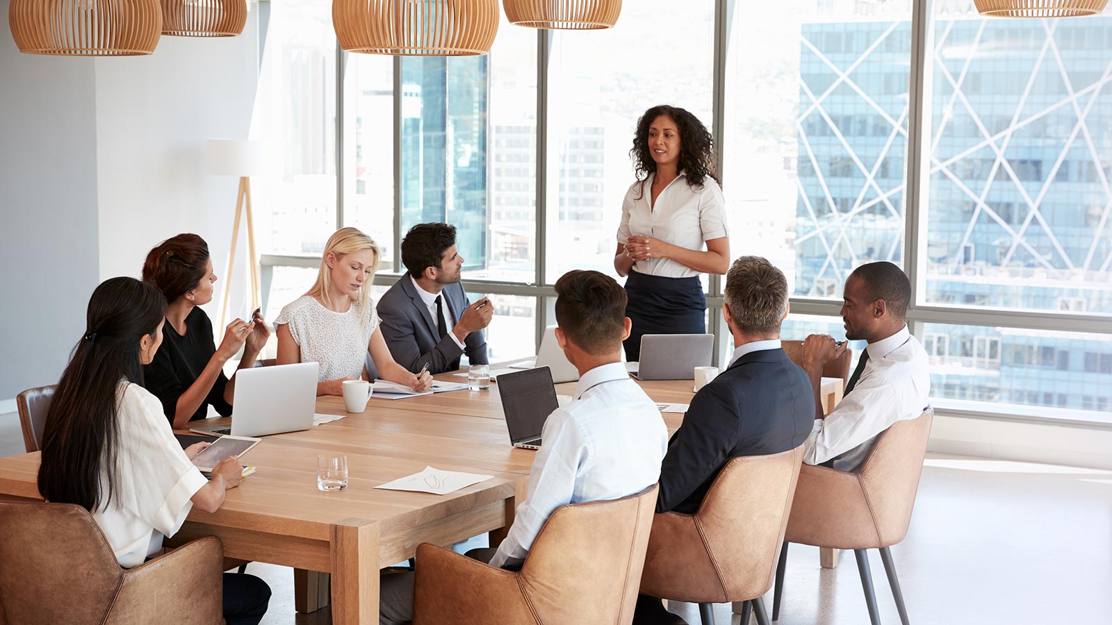 Businesswoman Stands To Address Meeting Around Board Table